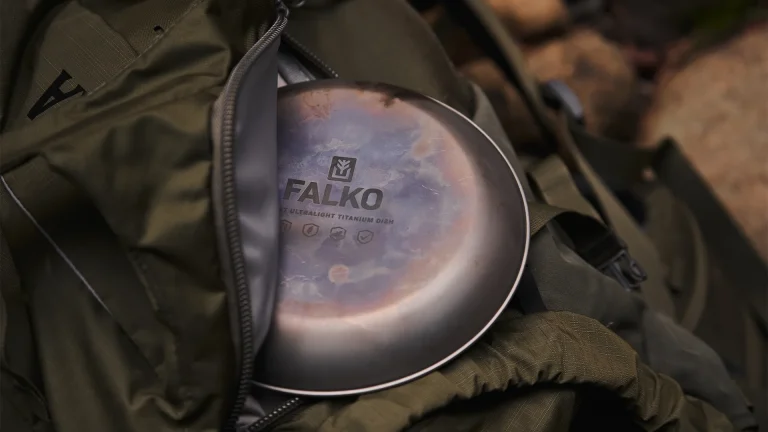 A titanium camping plate is sitting on top of hiking pack. Stains and marks show it has been well used.