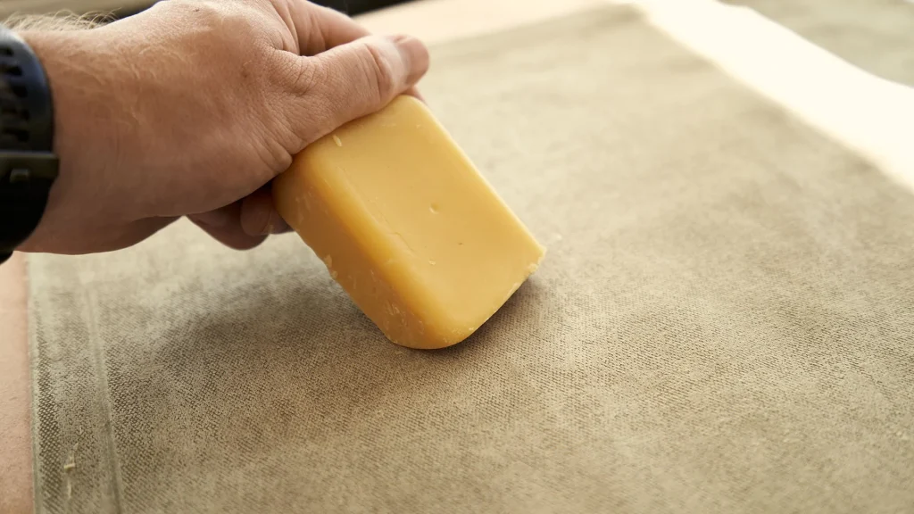 A beeswax bar being applied to canvas fabric in order to return waterproof abilities