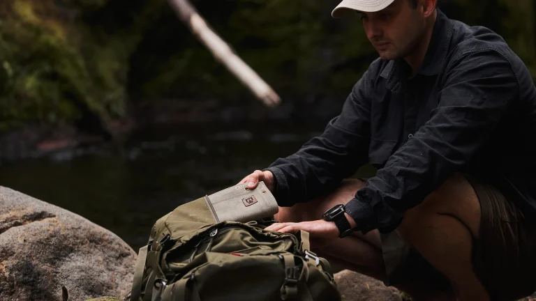 Outdoorsman crouches to pull waxed canvas ground mat from hiking pack